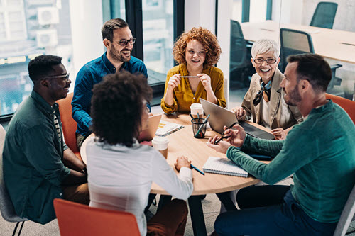 Screenshot of several people working and talking around a table.